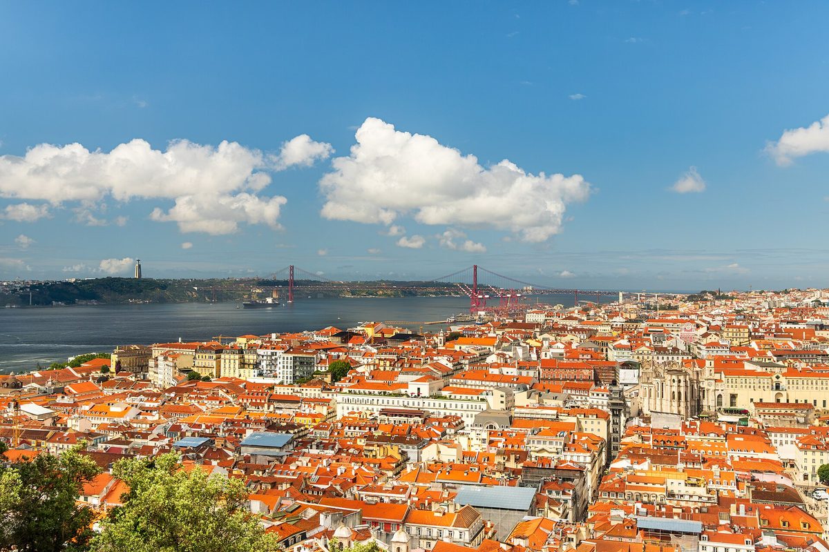 Terracotta rooftops of central Lisbon stretching to the Tagus River and the red 25 de Abril Bridge, seen from São Jorge Castle