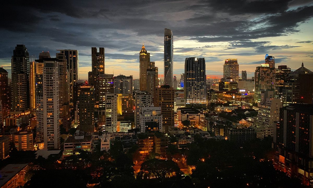 Bangkok's Ratchadamri district skyline at twilight, with lit towers under a dark, cloudy sky
